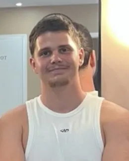 Portrait d’Ilian, coach sportif, léger sourire, en débardeur blanc dans une salle de sport