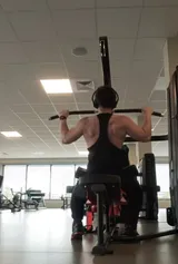 Ilian de dos, en débardeur noir, en plein tirage vertical dans une salle de sport